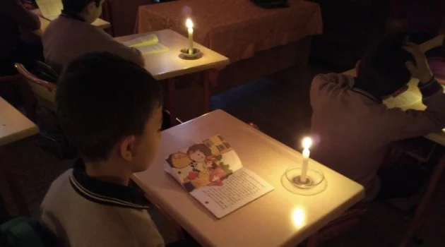 Minik öğrenciler mum ışığı eşliğinde kitap okuyor